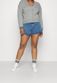 Szary bawełniany kardigan z zapięciem na guziki i czarnymi przeszyciami na mankietach, w połączeniu z niebieskimi szortami. Białe sneakersy i pasiasty skarpetki.