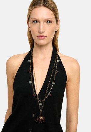 Czarny dzianinowy top na szyję z głębokim dekoltem w kształcie litery V i guzikami, ozdobiony warstwowo ułożonymi złotymi łańcuszkami z kolorowymi zawieszkami w kształcie słoni oraz centralną zawieszką słonia.