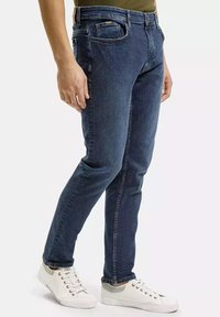 Ciemnoniebieskie dżinsy o slim fit, z pięcioma kieszeniami i widocznym szyciem. Połączone z białymi trampekami dla casualowego wyglądu.