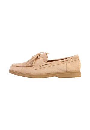 Mocassin en daim beige avec un nœud en dentelle à l’avant, œillets dorés et semelle plate en caoutchouc, présenté de côté sur fond blanc.