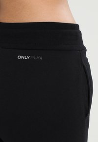 Zwarte sportbroek met een gestructureerde stof, elastische tailleband, zijzakken en een klein wit "ONLY PLAY"-logo aan de voorkant.