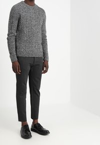 Grå texturerad tröja med rund halsringning, kombinerad med svarta byxor med tunna ränder och svarta snörskor. Enkel och modern design.