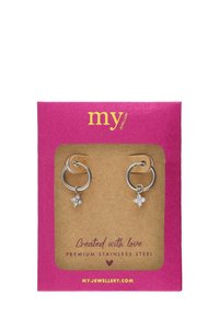 Pendientes de aro de acero inoxidable premium con pequeños charms de cristal claro, mostrados en una tarjeta texturizada de color rosa y dorado.