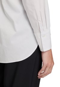 Witte blouse met lange mouwen gemaakt van gladde stof, met een knoopmanschette en een licht gebogen zoom, gecombineerd met zwarte broek.