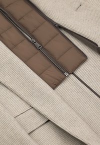 Beżowy materiał w paski na zewnątrz z brązową pikowaną podszewką wewnętrzną. Posiada centralny zamek błyskawiczny do zapinania. Wykończony ciemnobrązową lamówką.