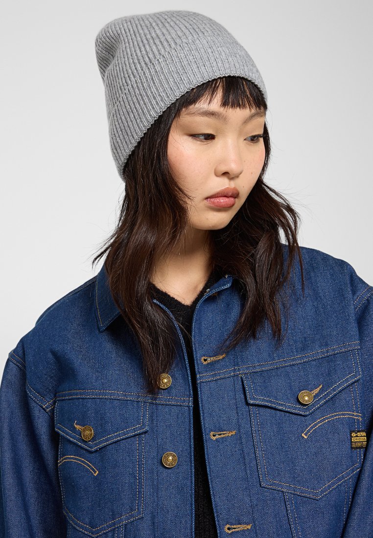 Szary, prążkowany czapka beanie, dopasowany kształt. Noszona z ciemną kurtką z złotymi guzikami i teksturowanym materiałem. Prosty, casualowy styl.
