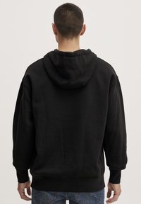 Sudadera negra con capucha, que presenta una gran capucha, puños y dobladillo de canalé, con una textura suave. La vista trasera muestra un ajuste relajado y holgado.