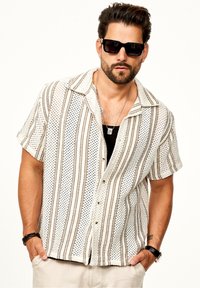 Kurzarmhemd aus weißem Stoff mit braunen vertikalen Streifen und Punkten. Der Kragen ist offen mit Knöpfen auf der Vorderseite.