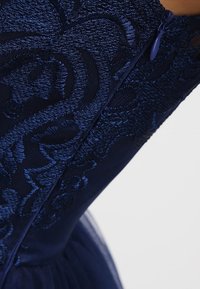 Tmavě modrá látka s propracovanou květinovou výšivkou a odpovídajícím modrým zipem na přiléhavých šatech nebo oděvu.