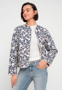 Veste à motif floral bleu et blanc, sans col, manches longues et poches avant, confectionnée en tissu léger.