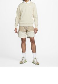 Ljusbeige sweatshirt med Nike-logotyp, tillsammans med beige och off-white färgblockerade shorts. Vita strumpor och beige camouflaged sneakers fulländar outfiten.