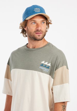 T-shirt coloré en blocs vert, beige et blanc avec logo ; tissu en coton doux ; casquette en velours côtelé bleu assortie avec visière beige et logo.