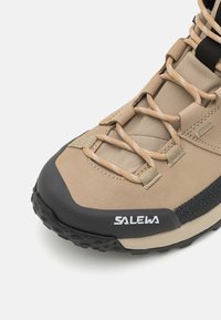 Scarpa da trekking beige con suola in gomma nera, caratterizzata da un design con lacci, materiale superiore resistente e lato testurizzato per una presa migliore. Include logo.