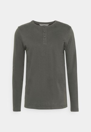 Camisa henley de manga larga en algodón verde oscuro. Presenta un escote redondo, una tapeta de cuatro botones y un estilo ajustado con textura suave.