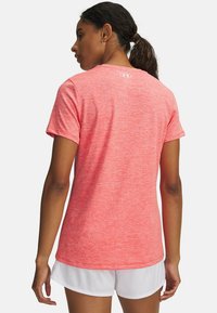 Camiseta deportiva de manga corta y cuello redondo en color coral jaspeado, confeccionada con tela ligera, con un sutil logo en la parte trasera. Combina con pantalones cortos blancos.