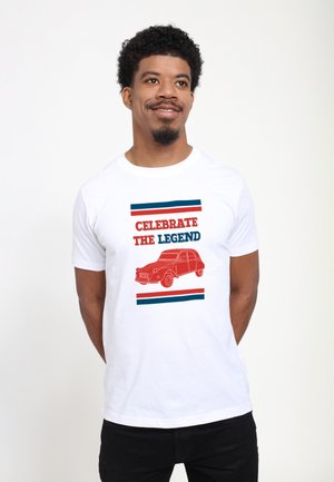 Hvid t-shirt med et rødt grafisk motiv af en vintage bil, med teksten "FEJR LEGENDEN" ovenfor og farvede striber nedenfor.
