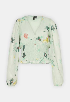 Bluza s cvjetnim uzorkom u mint zelenoj boji, s napuhanim rukavima, V-izrezom i nabranoj struku. Sadrži detalj s gumbima sprijeda i volanasti rub.