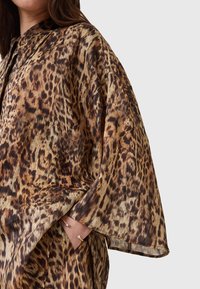 Camicia con stampa leopardata dal morbido e setoso texture. Presenta una vestibilità ampia, colletto e maniche larghe. I colori includono tonalità di marrone, nero e beige.