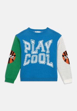 Barn genser med lange ermer, blå kropp med teksten "PLAY COOL", grønn venstre erme, hvit høyre erme og basketballansikter på albuene.
