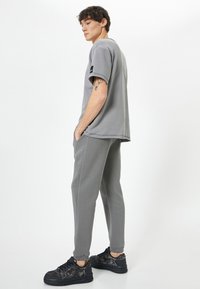 Szara bawełniana koszulka z krótkim rękawem, luźny krój. W połączeniu z dopasowanymi szarymi dresami i czarnymi, strukturalnymi sneakersami. Minimalistyczny design.