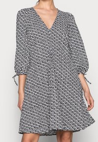 Šaty s černobílým vzorem, s výstřihem do V, nabíranými rukávy a šňůrkovými detaily na manžetách. Rozšířený střih, lehký materiál.