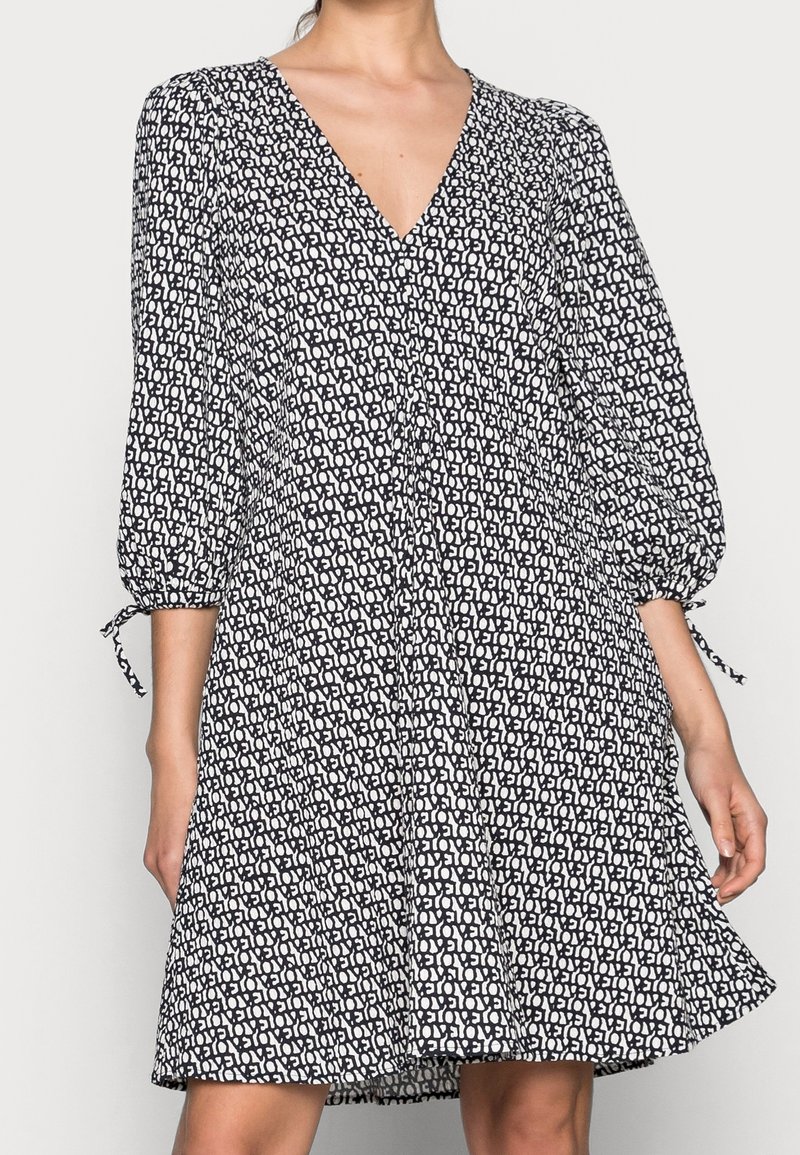 Šaty s černobílým vzorem, s výstřihem do V, nabíranými rukávy a šňůrkovými detaily na manžetách. Rozšířený střih, lehký materiál.