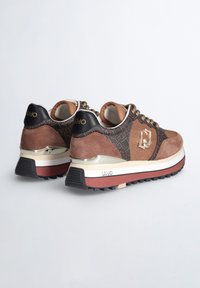 Sneaker marroni con un mix di camoscio e rete, dotati di hardware dorato, un design a motivo e una spessa intersuola bianca accentuata con rosso.