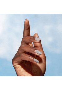 Hand met een verzorgde uitstraling, met lichtgrijze nagellak op langgerekte, slanke vingers tegen een zachte blauwe achtergrond.