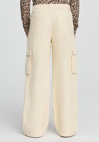 Beżowe szerokie spodnie cargo o luźnym kroju, z bocznymi kieszeniami, miękką teksturą i elastycznym paskiem w talii.