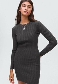 Robe à manches longues côtelée de couleur gris foncé. Design ajusté, col rond, tissu texturé. Présente un collier en pendentif argent minimaliste.