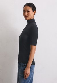 Zwarte geribbelde top met korte mouwen en hoge hals, strak ontwerp en een gladde textuur, gecombineerd met lichtblauwe denim.