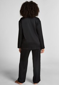 Zwart satijnen loungewear set met een streeppatroon, lange mouwen top en brede pijpen met een ontspannen pasvorm. Glad textuur, minimalistisch ontwerp.
