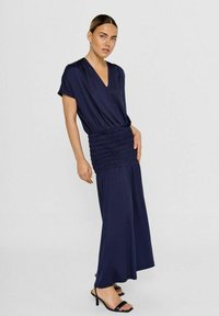 Marineblauw jurkje met een V-hals, korte mouwen, gerimpelde taille en vloeiende rok. De stof lijkt zacht met een gladde textuur.