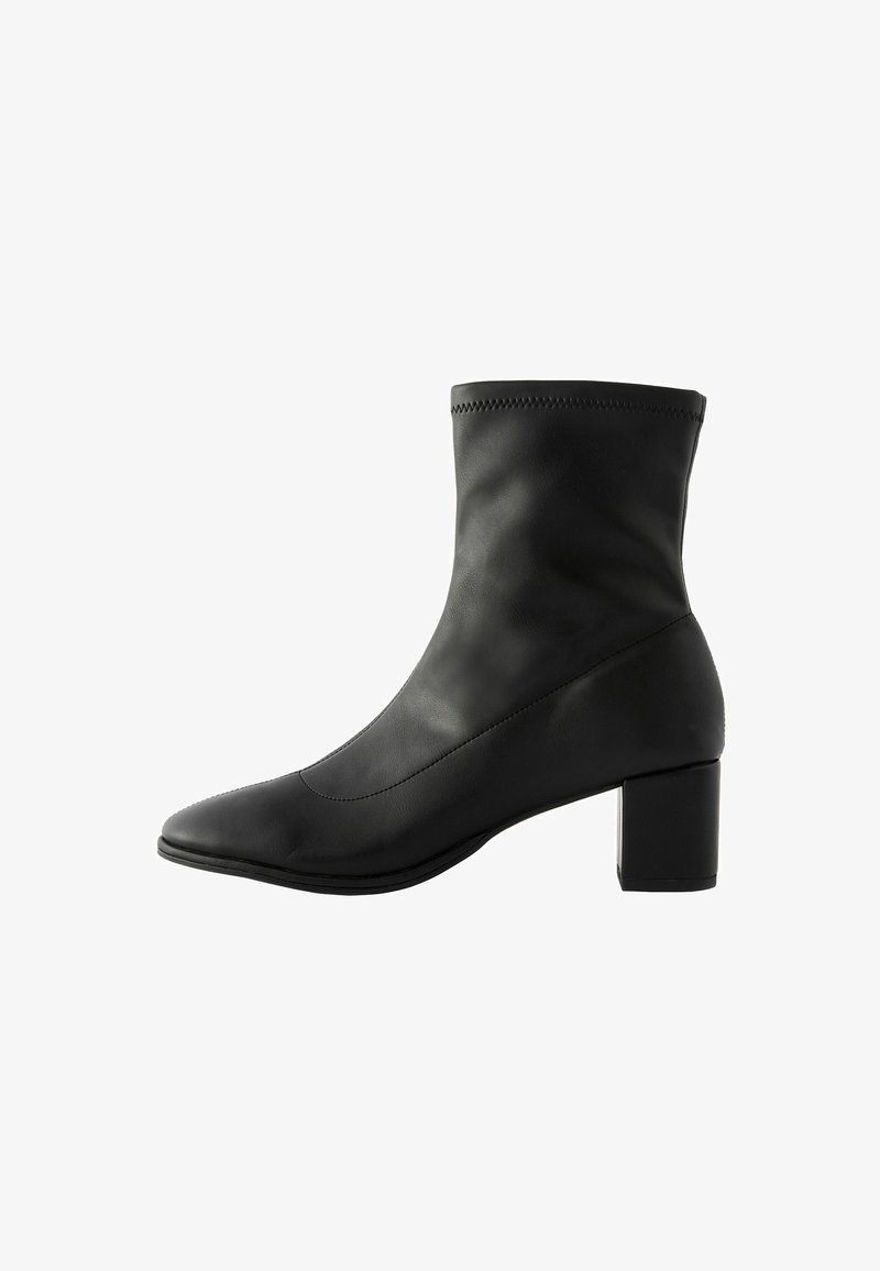 Botte chevillère noire en cuir lisse avec un bout pointu, un talon moyen et un subtil surpiquage le long du bord supérieur.