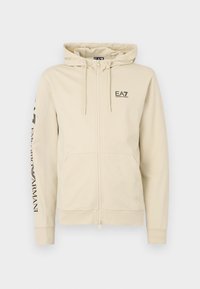 Licht beige hoodie met rits van zacht materiaal. Voorzien van een capuchon met trekkoord, twee zakken aan de voorkant en een logo op de borst en mouw.