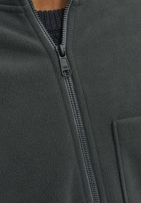 Tmavě šedá fleecová bunda s celopropínacím zipem, texturovaným materiálem a kapsou na hrudi. Zip je černý s hladkým jezdcem.