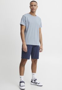 Lys blå bomulls-T-skjorte med rund hals, kombinert med marineblå cargo-shorts. Tilbehøret inkluderer hvite sokker og marineblå joggesko.