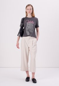 Grijze katoenen t-shirt met een luipaardafdruk en de tekst "Wild", gecombineerd met crèmekleurige wijde broeken en zwarte loafers. Zwarte handtas inbegrepen.