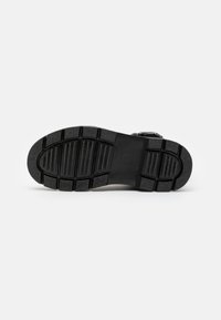 Black shoe sole with a textured rubber surface, featuring horizontal and vertical grooves for traction, and reinforced edges.