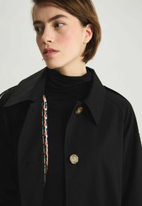 Manteau noir avec un grand col, fermeture à un bouton unique et une doublure intérieure à motif coloré. Texture lisse et design élégant.