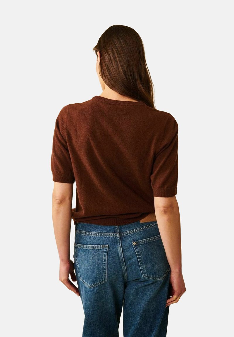 Ruskea lyhythihainen neulepaita pyöreällä kaula-aukolla, päälläsinisen farkkuhousujen kanssa, joissa on takataskut, esitetty takaa.