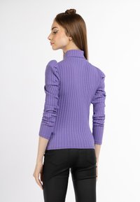 Lila gerippter Langarmoberteil mit hohem Kragen und gepufften Schultern, kombiniert mit schwarzen eng anliegenden Hosen. Glatte Textur, figurbetontes Design.