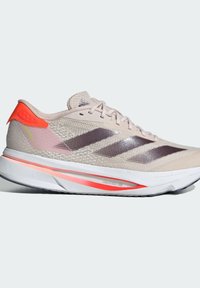 Chaussure de course légère beige avec tige en mesh, accents gris et talon orange fluo. Présente un design distinct à trois bandes et une semelle rembourrée.