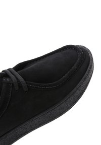 Zapato de ante negro con cuello acolchado, cierre de cordones y suela de goma texturizada para mayor agarre. Superficie suave con detalles cosidos.