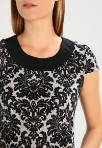 Haut à manches courtes noir et gris avec un motif floral, col rond noir uni et tissu texturé.