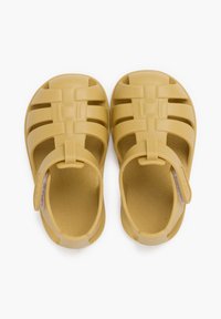 Chanclas de goma amarillas con la puntera cerrada, correa en el talón y diseño abierto. Presentan una plantilla texturizada con un patrón en espiral.
