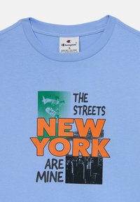 Ljusblå bomulls-t-shirt med grafisk tryck som har texten "STREETS NEW YORK ÄR MINA" i orange och svart, tillsammans med en bild av en skateboardåkare.