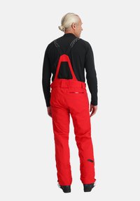 Rote Skihosen mit verstellbaren Trägern, einem Mesh-Bereich auf der Rückseite und einem schlanken, wasserdichten Design. Enthält verstärkte Nähte und mit Reißverschlüssen versehene Taschen.