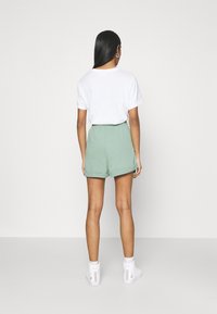 Bílá tričko a zelené šortky s ohrnutým lemem, kombinované s bílými teniskami. Oblečení má volný střih a je vyrobeno z měkkého materiálu.