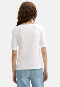 Witte T-shirt met korte mouwen, ontspannen pasvorm en wijde halslijn, gemaakt van een lichtgewicht stof, gedragen met lichtblauwe jeans.